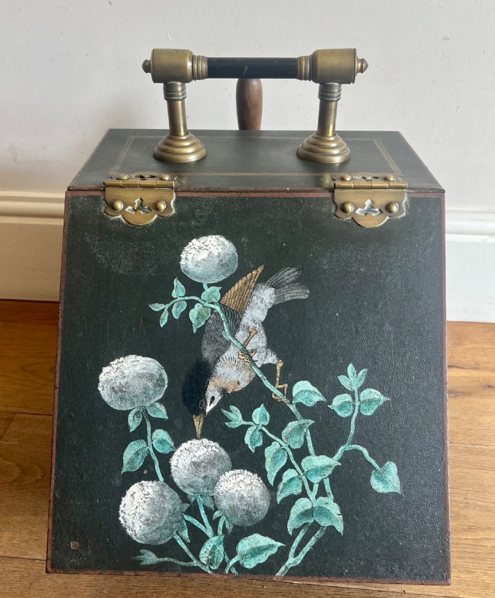 An antique dark green toleware coal scuttle featuring a slant front with a hand-painted bird and floral motif, brass hinges, and a brass top handle.