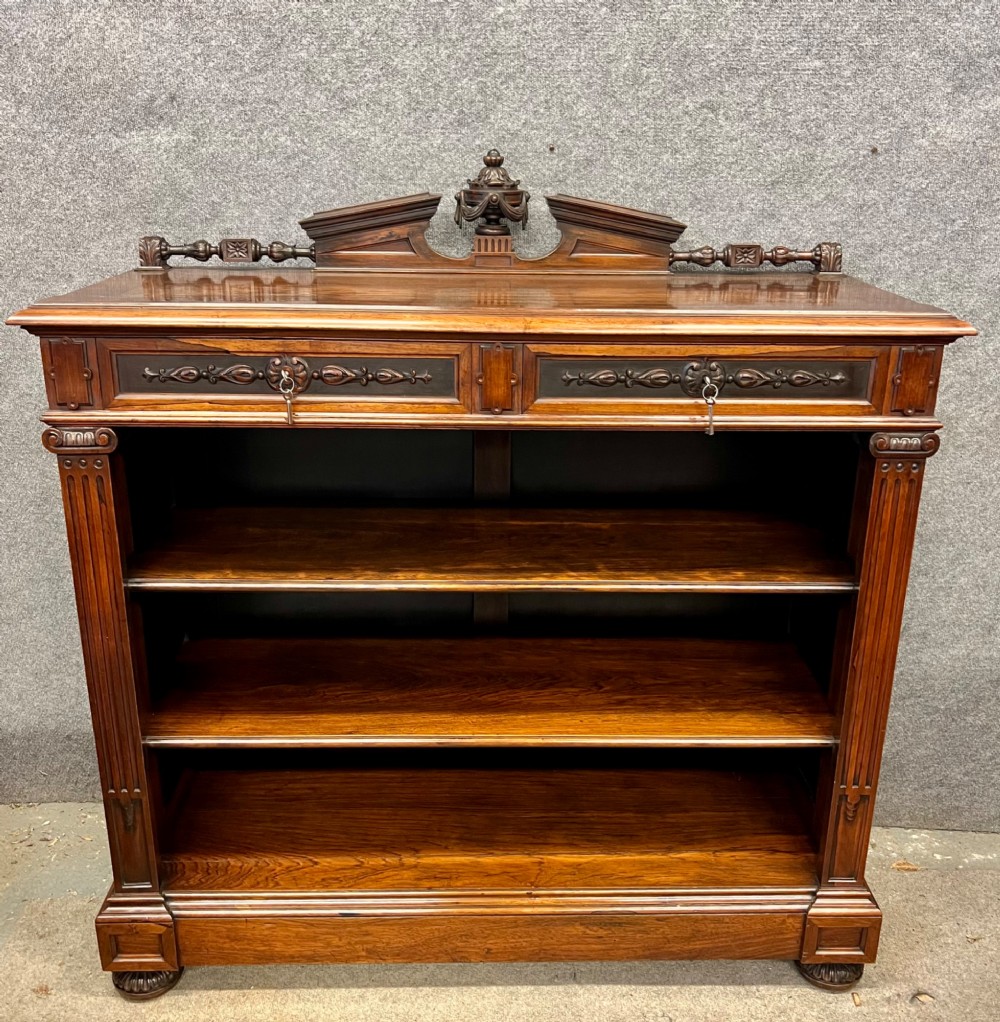 A Victorian dark walnut open bookcase with two carved drawers, open shelves, fluted pilasters, and a decorative pediment top featuring a central urn finial.