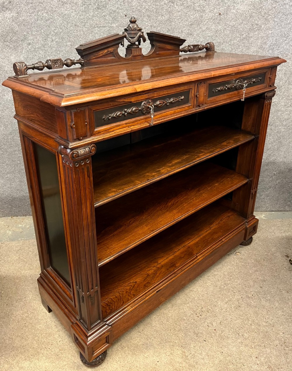 A Victorian dark walnut open bookcase with two carved drawers, open shelves, fluted pilasters, and a decorative pediment top featuring a central urn finial. View IV