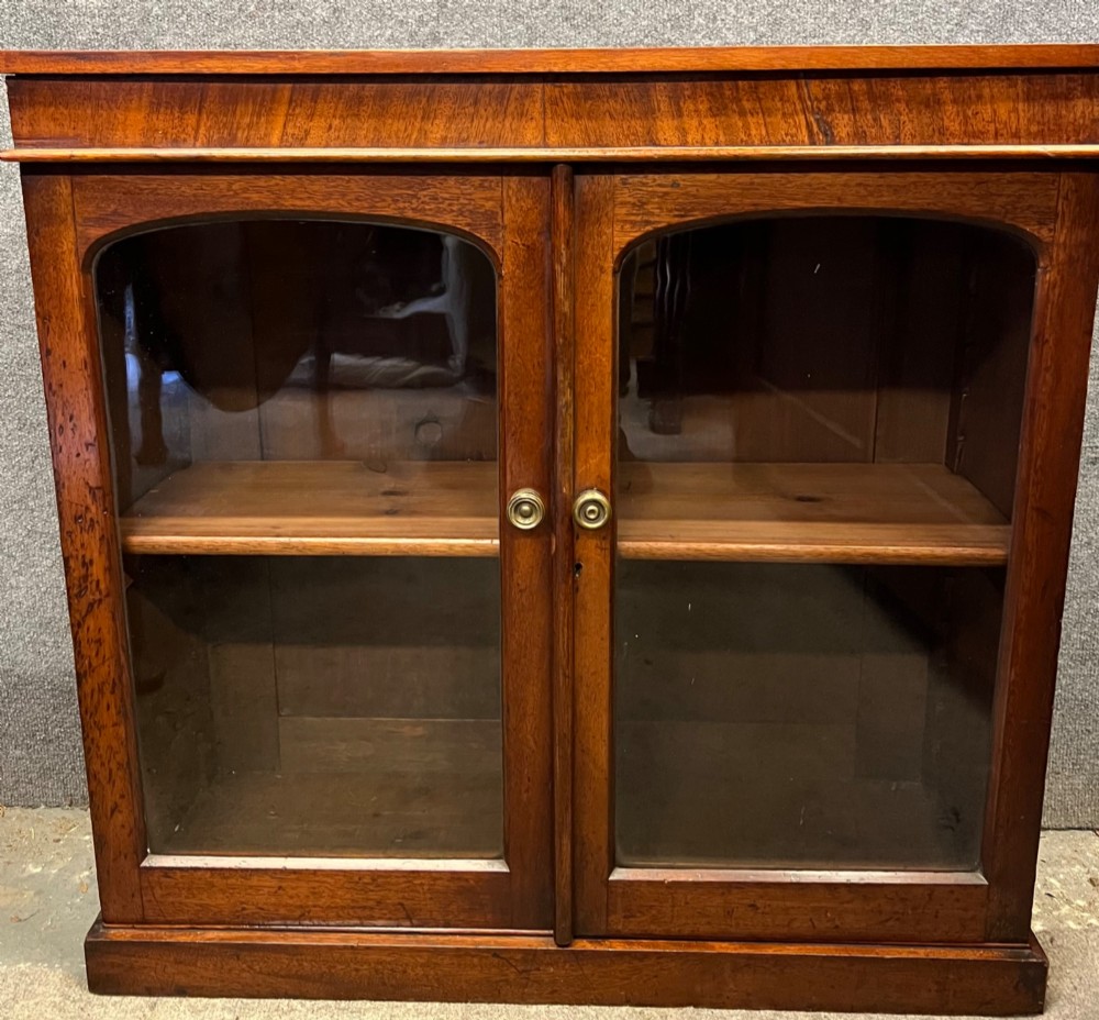 A small Victorian mahogany low bookcase featuring two glazed doors with arched frames, brass knobs, internal timber shelving, and a plinth base. View II