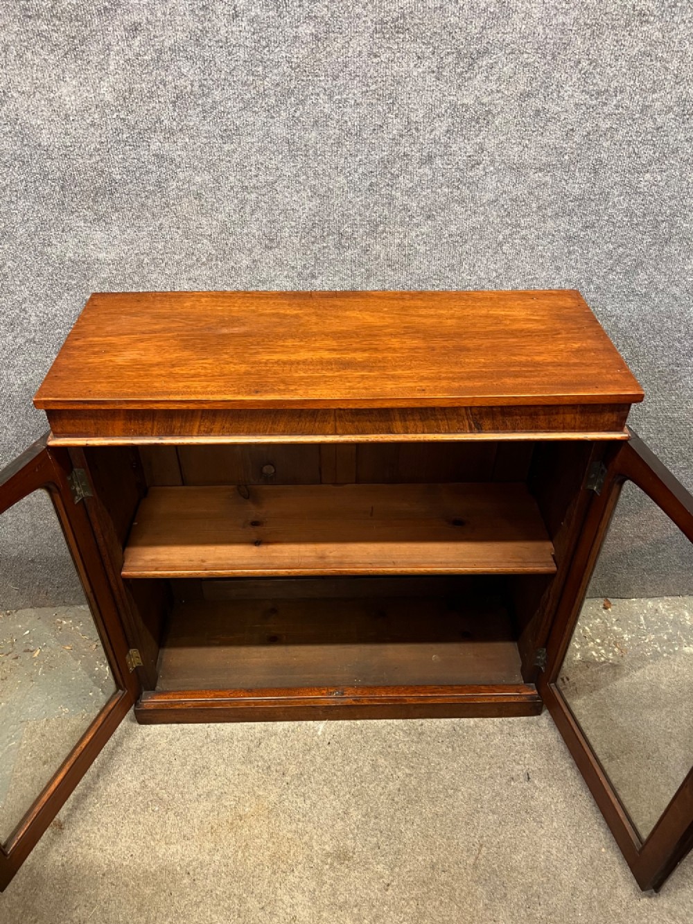 A small Victorian mahogany low bookcase featuring two glazed doors with arched frames, brass knobs, internal timber shelving, and a plinth base. View VII