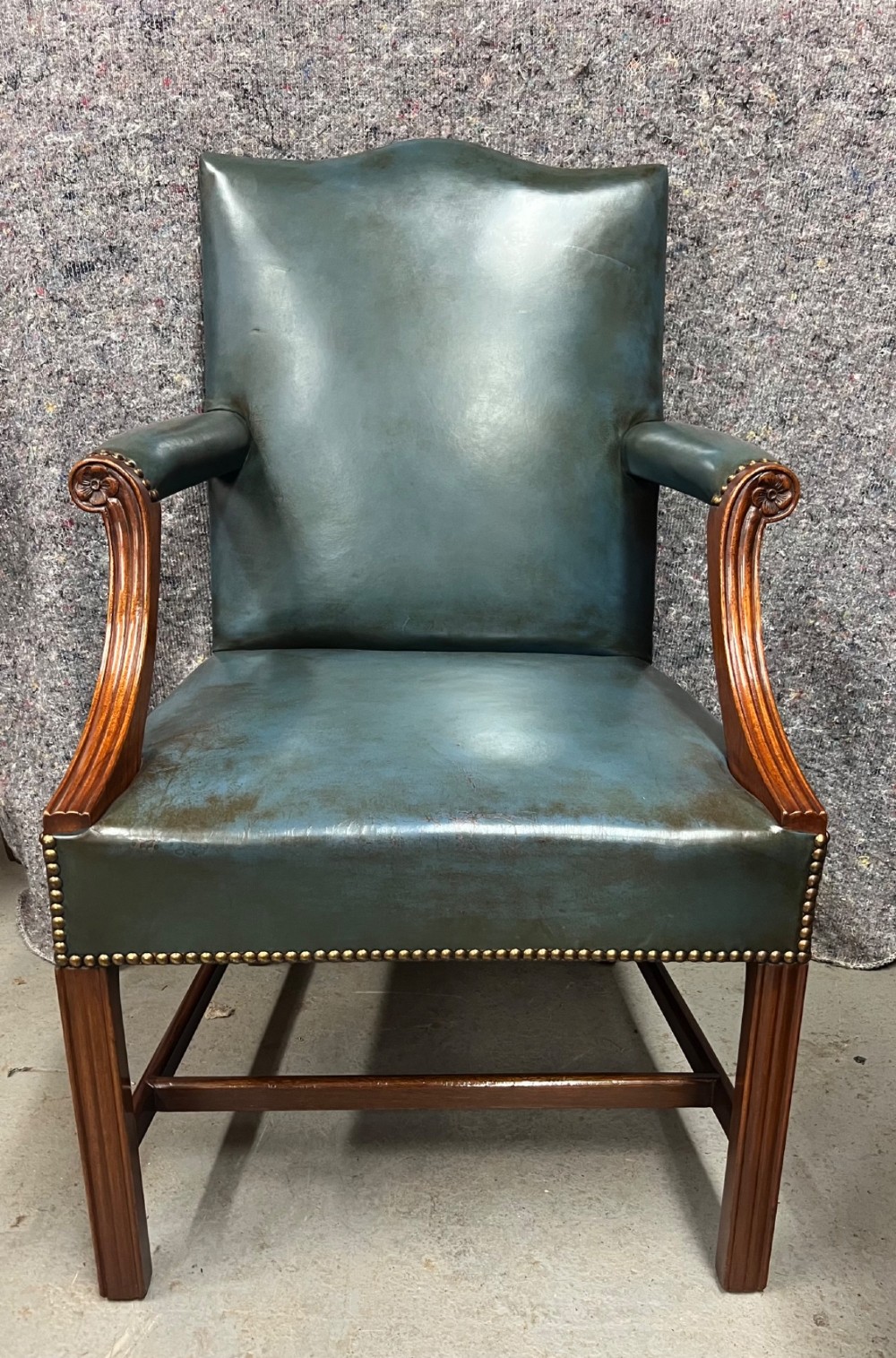 A Gainsborough style desk chair upholstered in patinated green leather with brass stud trimming and carved mahogany arm supports.