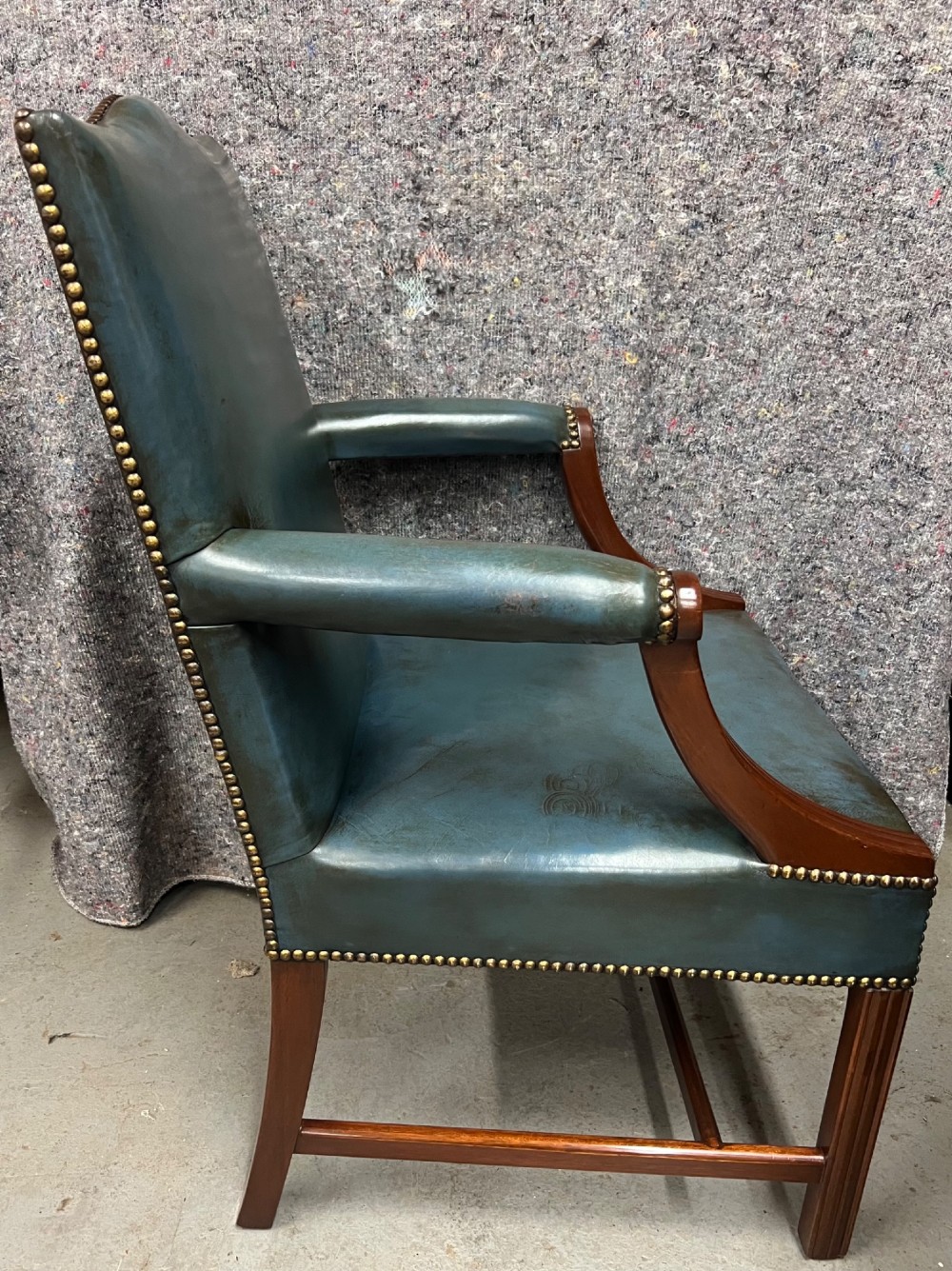 A Gainsborough style desk chair upholstered in patinated green leather with brass stud trimming and carved mahogany arm supports. View II