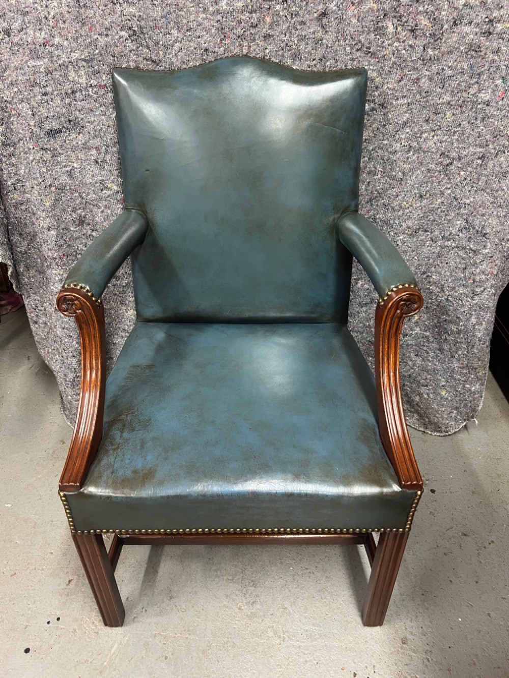 A Gainsborough style desk chair upholstered in patinated green leather with brass stud trimming and carved mahogany arm supports. View VI