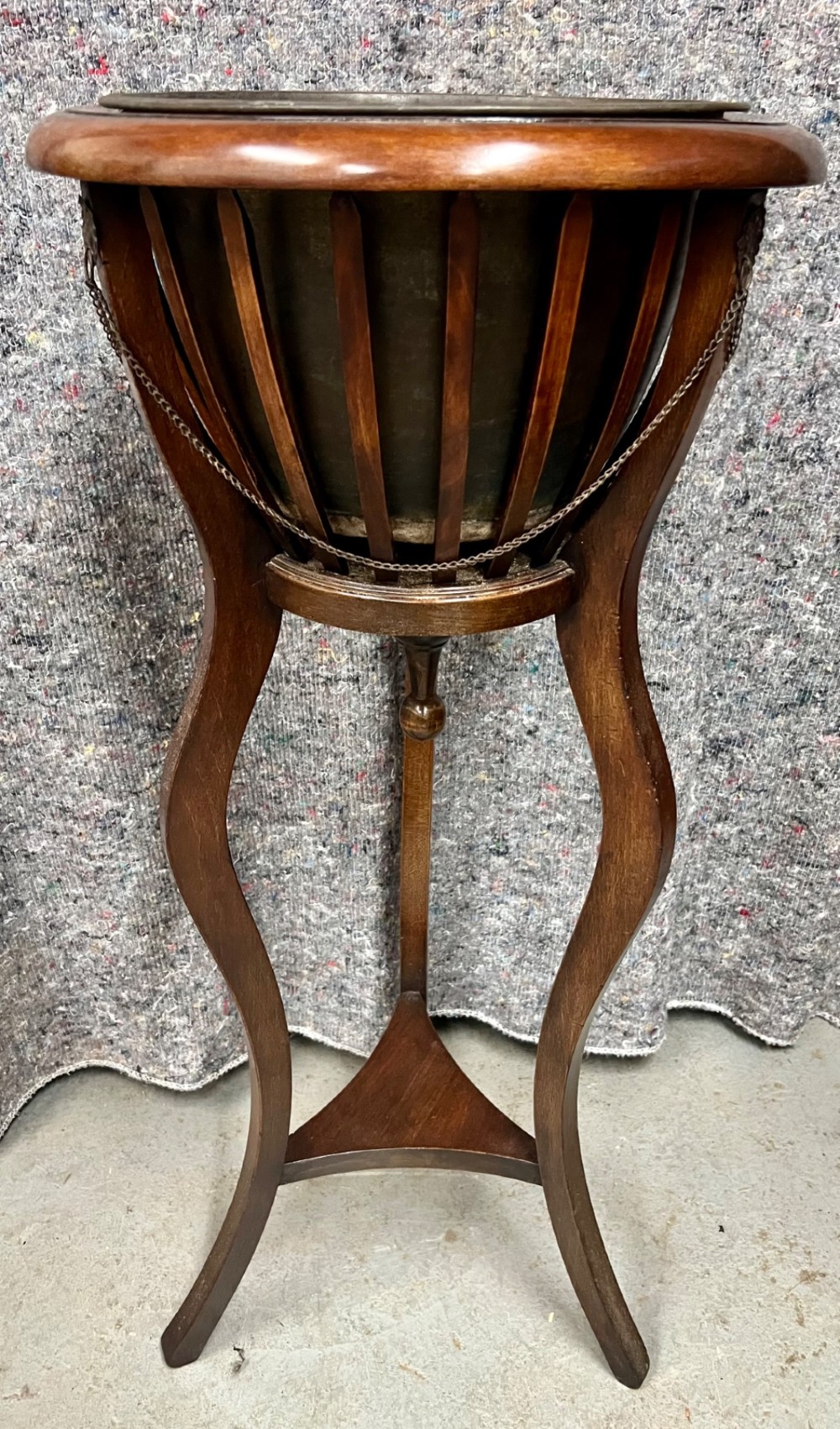 An Edwardian mahogany jardiniere plant stand featuring a slatted circular bucket with internal metal lining, supported by three curved legs and a triangular base stretcher.