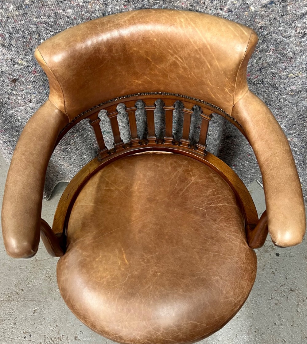 A Victorian mahogany revolving desk chair with tan leather padded seating, brass stud detailing, and a turned spindle gallery backrest. View II