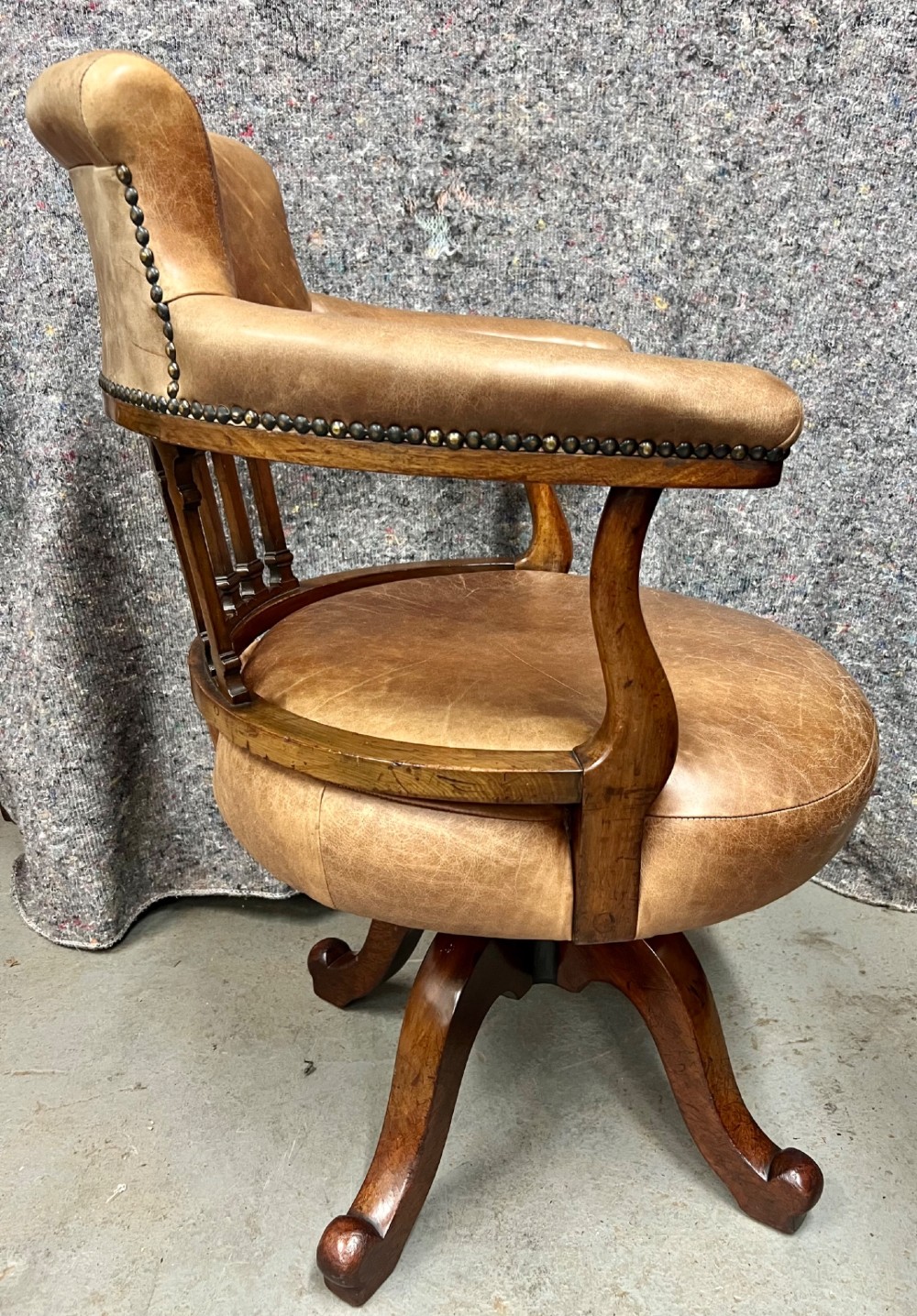 A Victorian mahogany revolving desk chair with tan leather padded seating, brass stud detailing, and a turned spindle gallery backrest. View IV