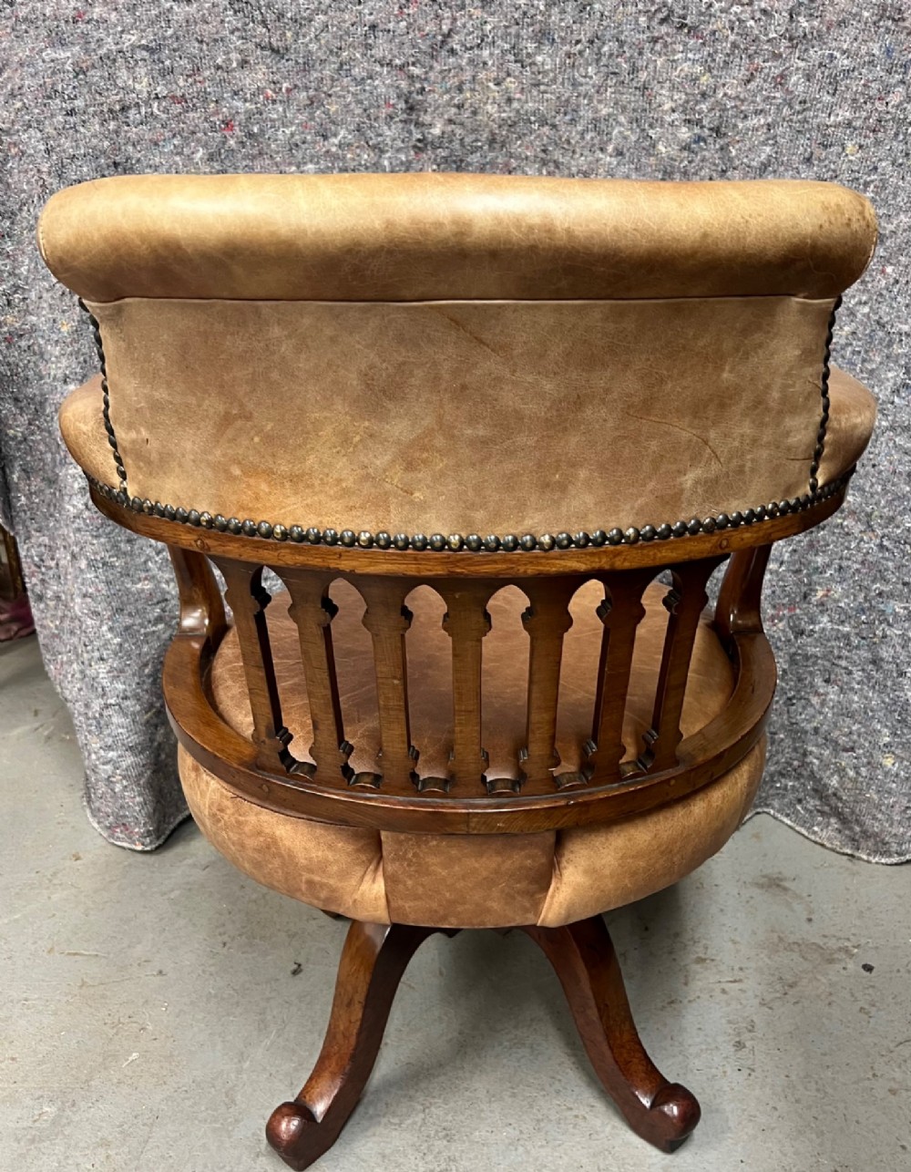 A Victorian mahogany revolving desk chair with tan leather padded seating, brass stud detailing, and a turned spindle gallery backrest. View V
