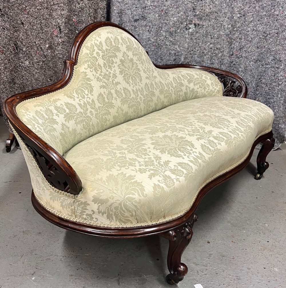 A Victorian small settee with a carved mahogany frame, pale green floral damask fabric, pierced arm supports, and cabriole legs on brass castors.