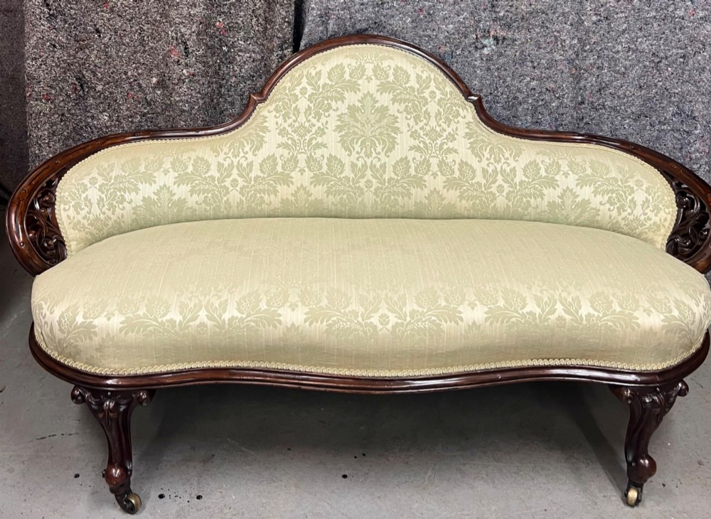 A Victorian small settee with a carved mahogany frame, pale green floral damask fabric, pierced arm supports, and cabriole legs on brass castors. View II