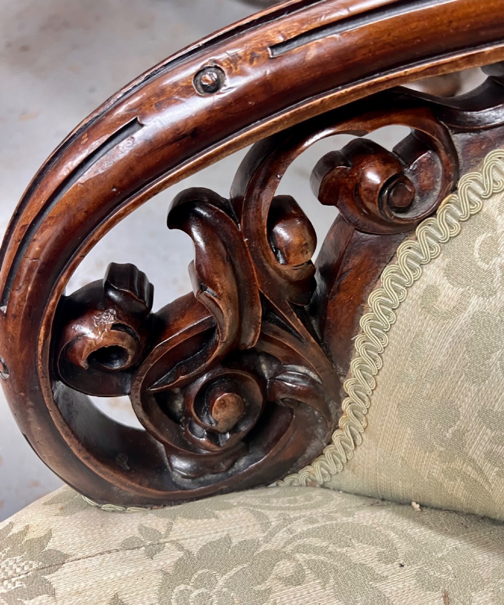 A Victorian small settee with a carved mahogany frame, pale green floral damask fabric, pierced arm supports, and cabriole legs on brass castors. View V