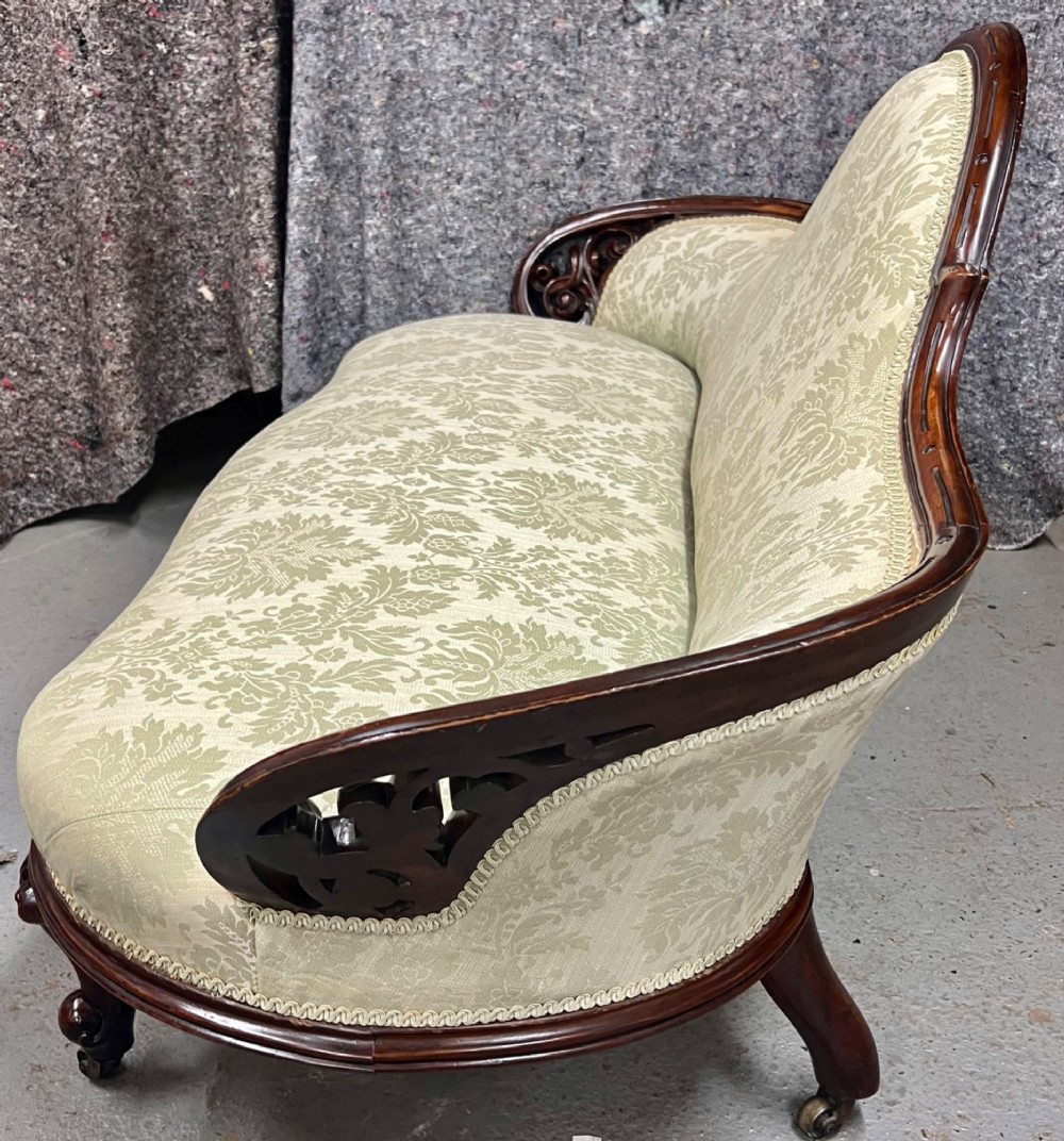 A Victorian small settee with a carved mahogany frame, pale green floral damask fabric, pierced arm supports, and cabriole legs on brass castors. View VII
