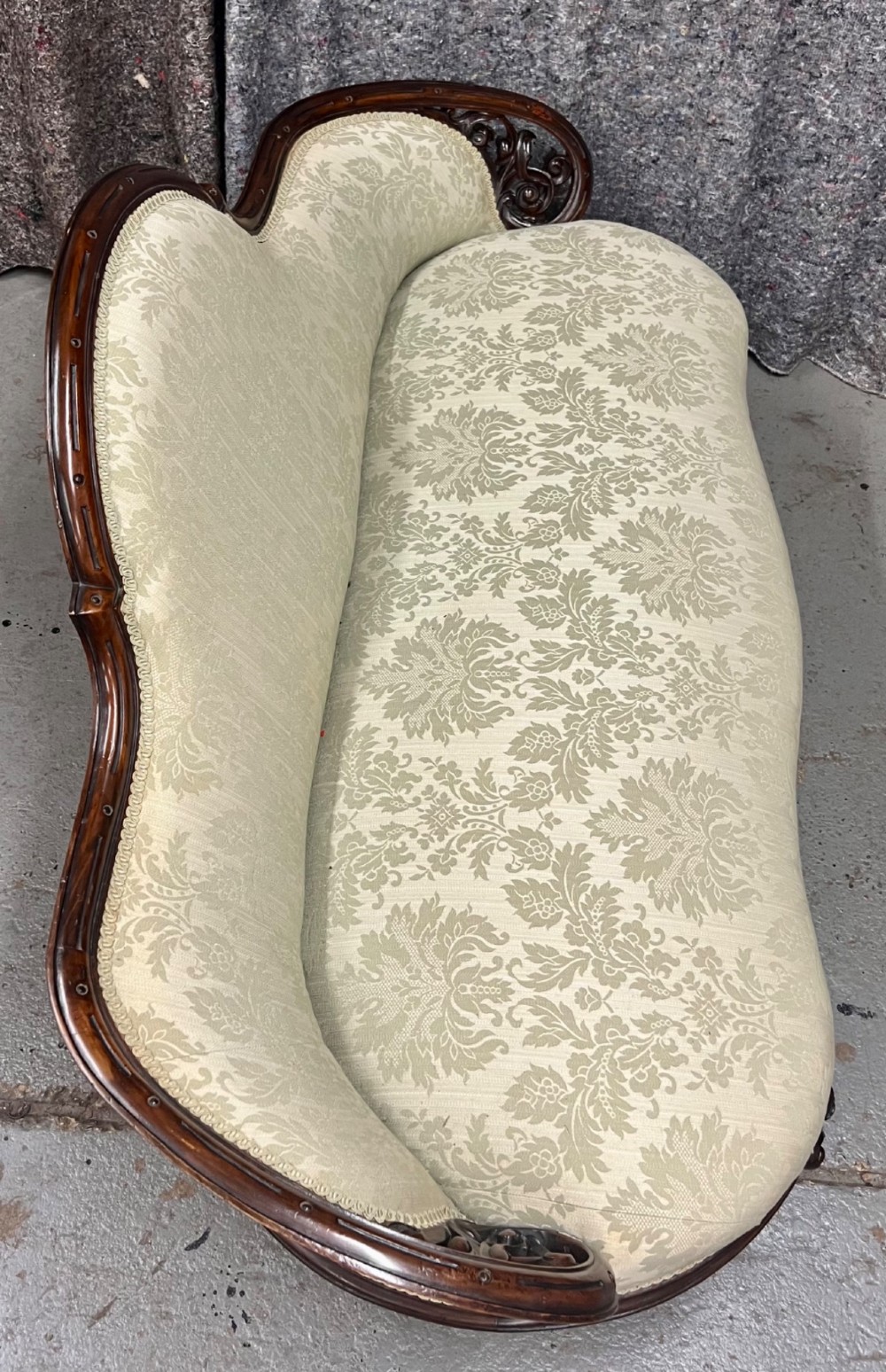A Victorian small settee with a carved mahogany frame, pale green floral damask fabric, pierced arm supports, and cabriole legs on brass castors. View IX