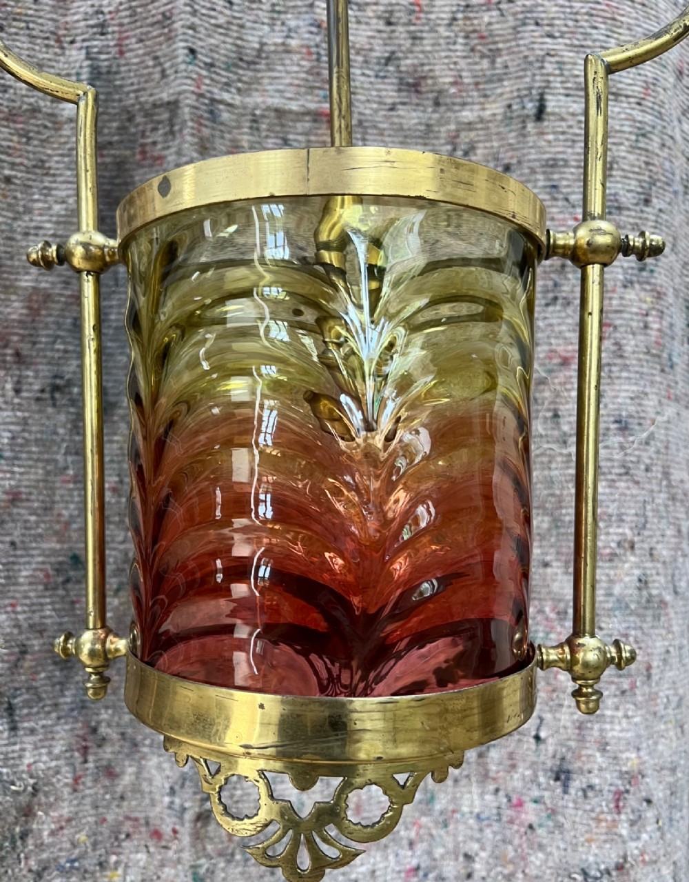 An antique brass hanging pendant lantern featuring a contoured brass frame suspending a moulded pink and amber glass shade. View II
