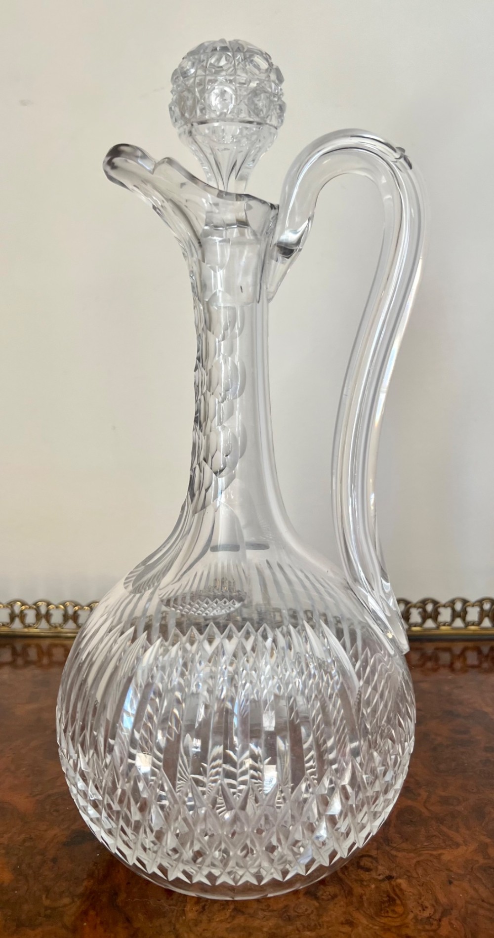 An Edwardian clear cut glass claret jug featuring a diamond-cut pattern body, an elongated handle, and a faceted spherical stopper.