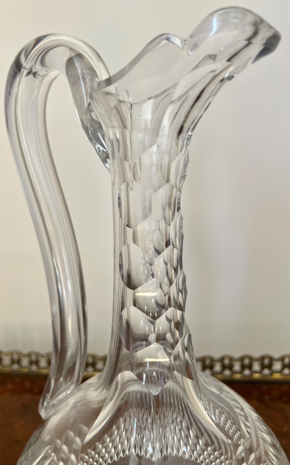 An Edwardian clear cut glass claret jug featuring a diamond-cut pattern body, an elongated handle, and a faceted spherical stopper. View V