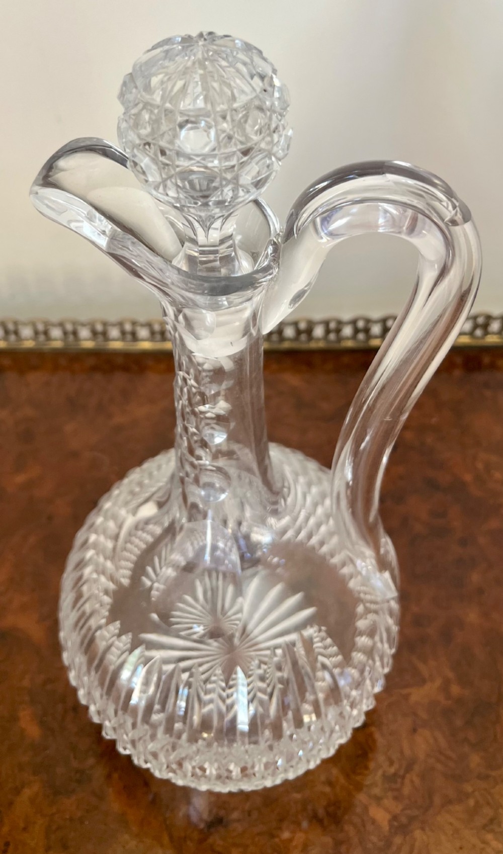 An Edwardian clear cut glass claret jug featuring a diamond-cut pattern body, an elongated handle, and a faceted spherical stopper. View VII