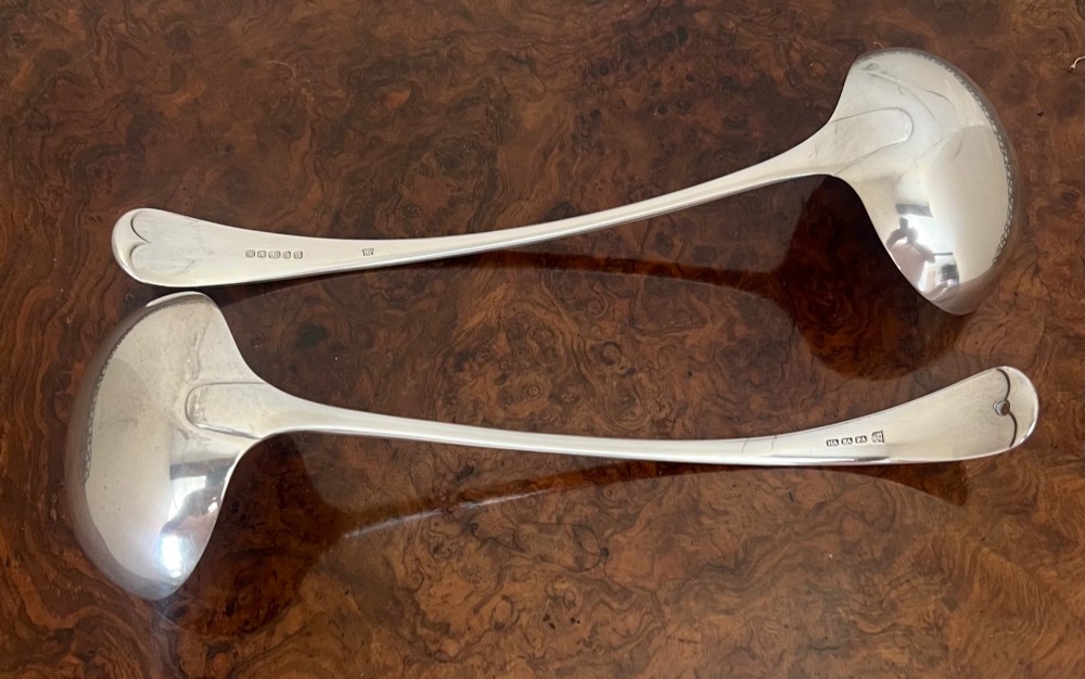 A matched pair of large silver-plated ladles with deep circular bowls and polished curved handles displayed on a wooden surface. View II