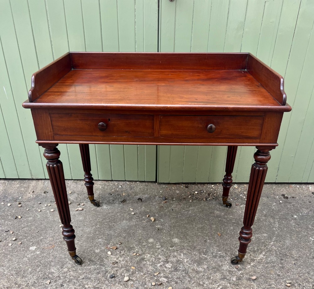 A nineteenth-century mahogany side table with a low gallery back, two frieze drawers, and turned reeded legs on brass castors. View II
