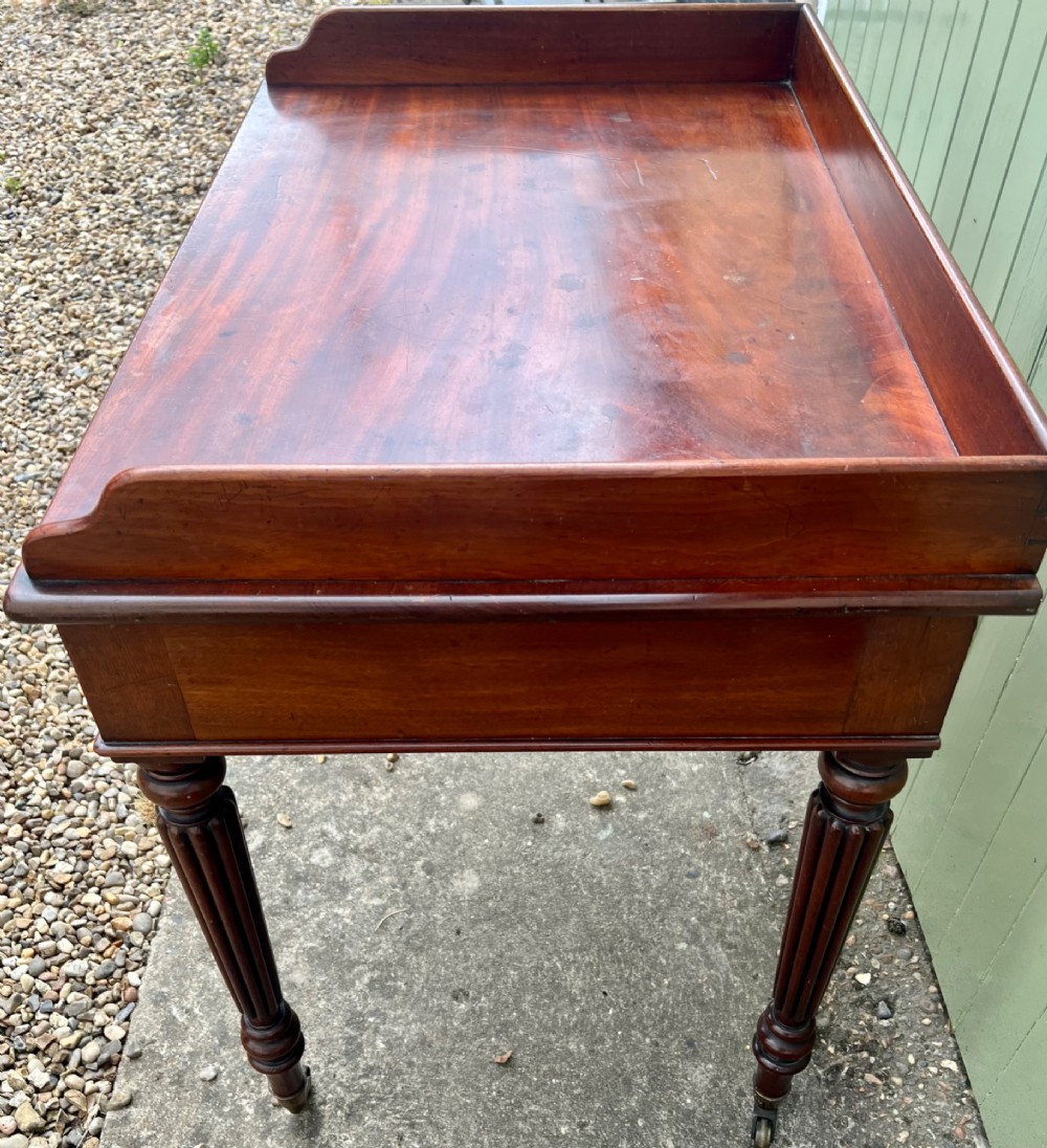 A nineteenth-century mahogany side table with a low gallery back, two frieze drawers, and turned reeded legs on brass castors. View III