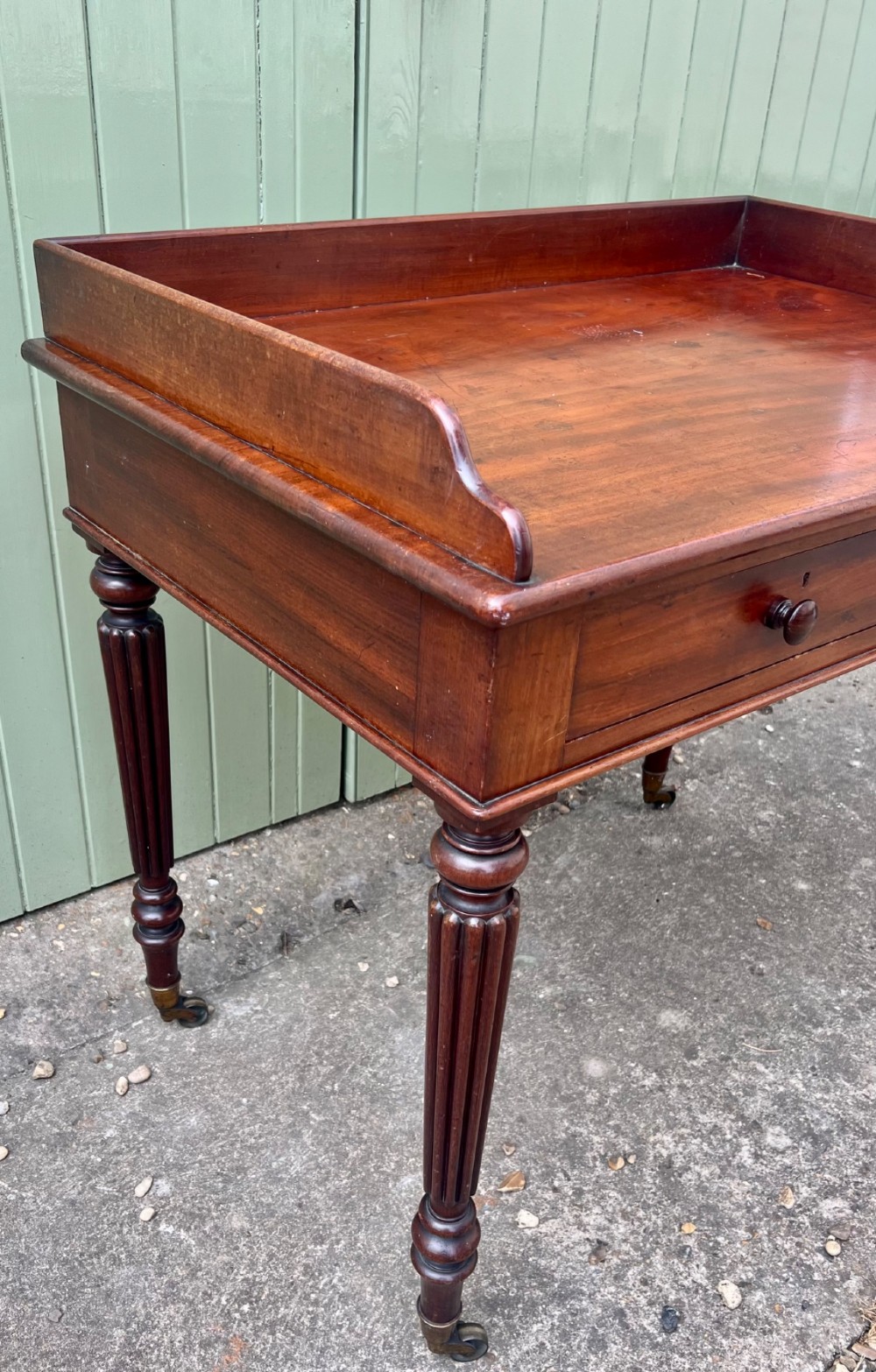 A nineteenth-century mahogany side table with a low gallery back, two frieze drawers, and turned reeded legs on brass castors. View VI
