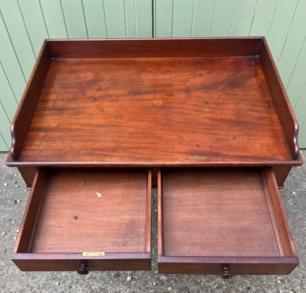 A nineteenth-century mahogany side table with a low gallery back, two frieze drawers, and turned reeded legs on brass castors. View XII