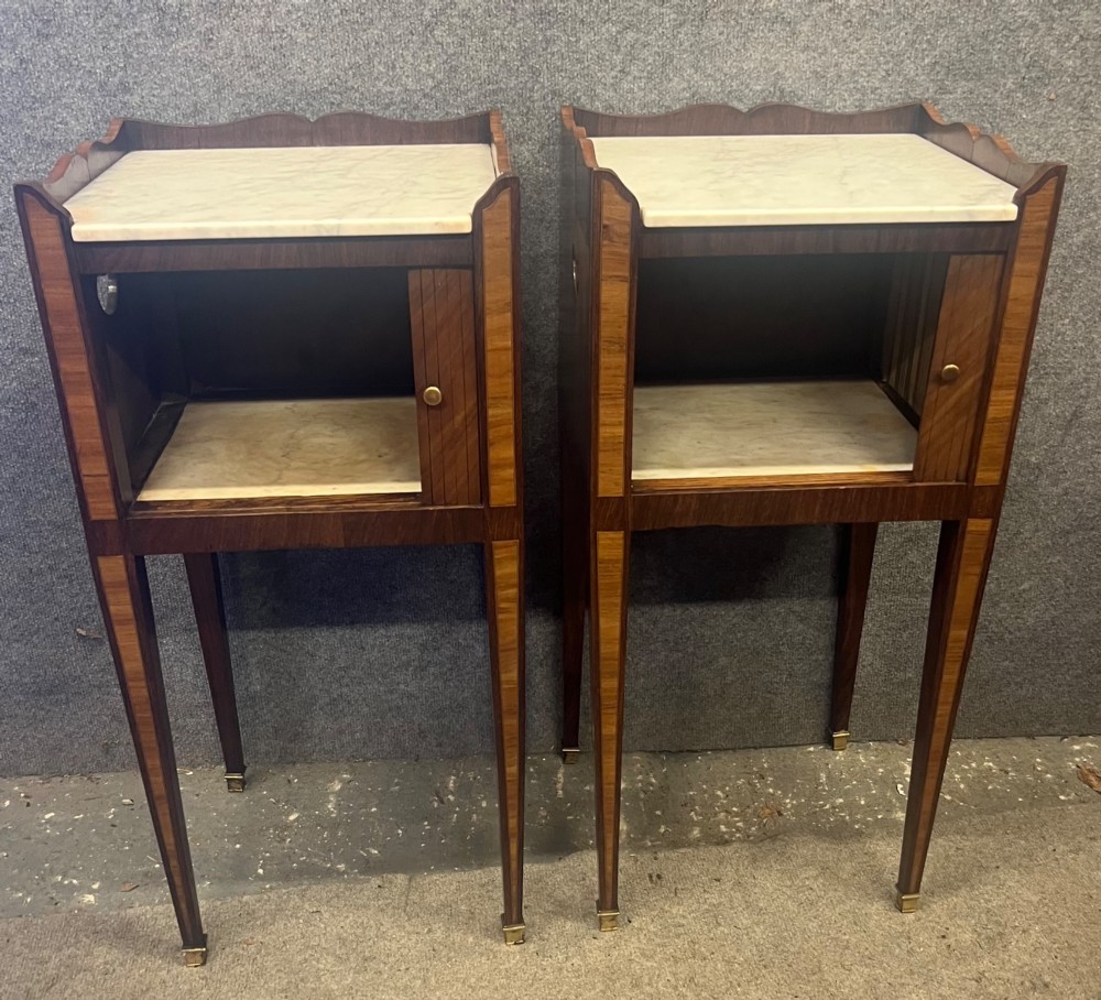 A pair of slender French bedside cabinets featuring chevron wood parquetry doors, white marble tops, and long tapered legs with brass feet. View II