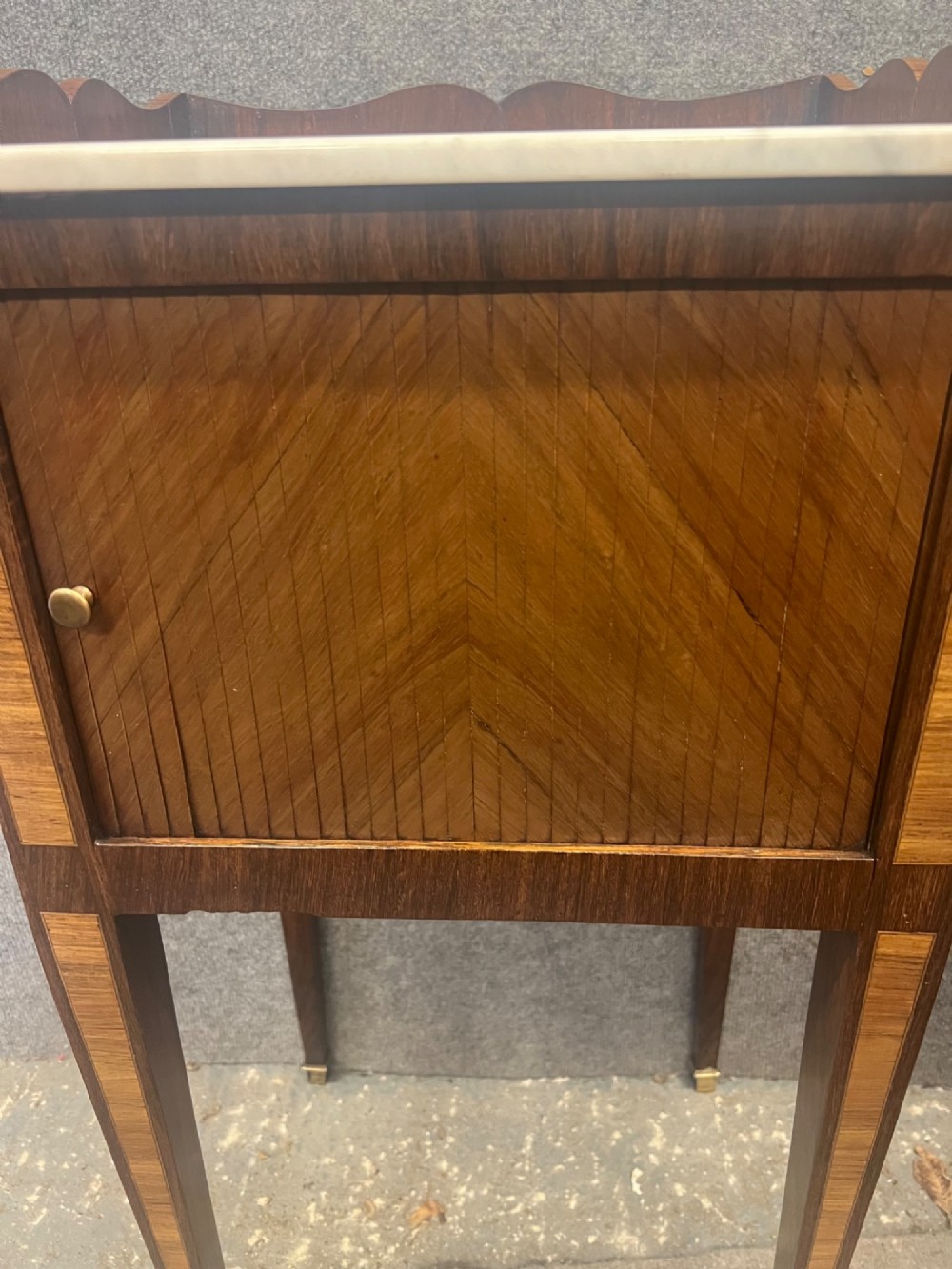 A pair of slender French bedside cabinets featuring chevron wood parquetry doors, white marble tops, and long tapered legs with brass feet. View VII