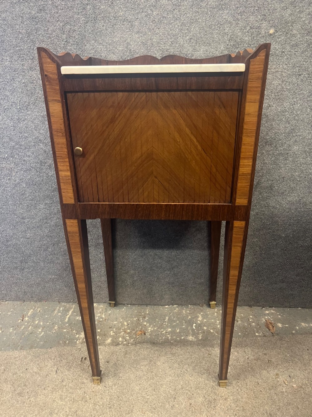 A pair of slender French bedside cabinets featuring chevron wood parquetry doors, white marble tops, and long tapered legs with brass feet. View IX