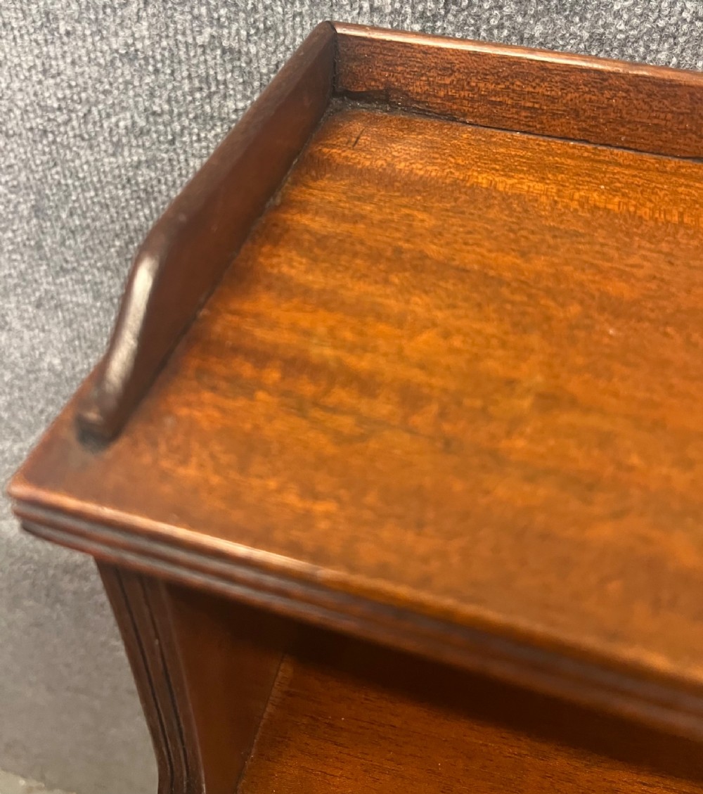 A warm mahogany open waterfall bookcase featuring three tiered shelves above twin drawers on turned legs with brass castors. View V