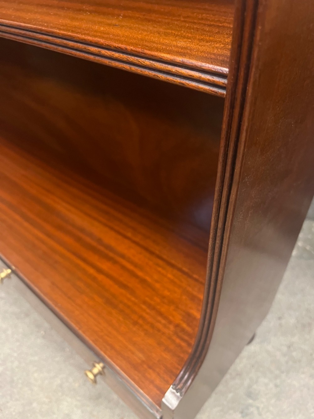 A warm mahogany open waterfall bookcase featuring three tiered shelves above twin drawers on turned legs with brass castors. View VI