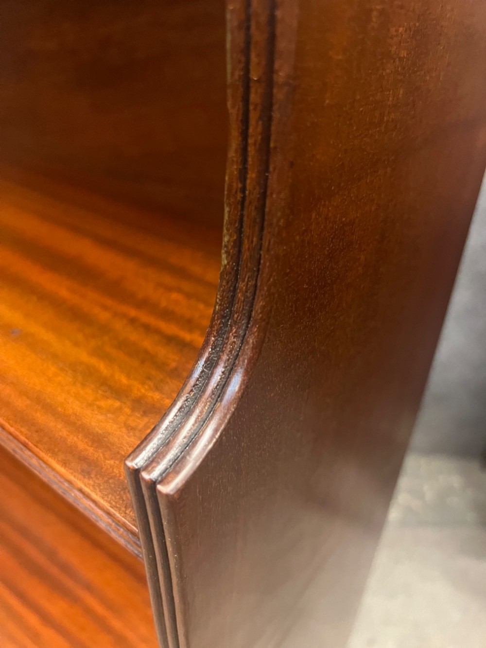 A warm mahogany open waterfall bookcase featuring three tiered shelves above twin drawers on turned legs with brass castors. View VII