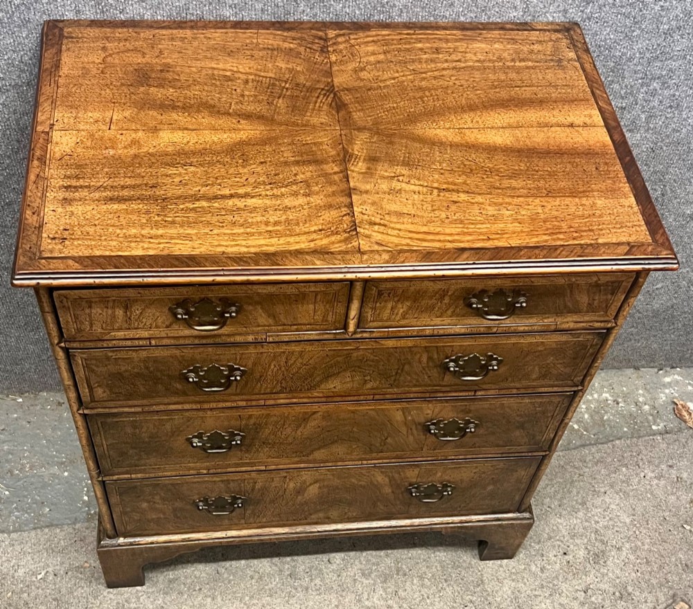 A small 18th-century style walnut chest of drawers featuring figured wood grain, brass drop handles, and bracket feet. View II