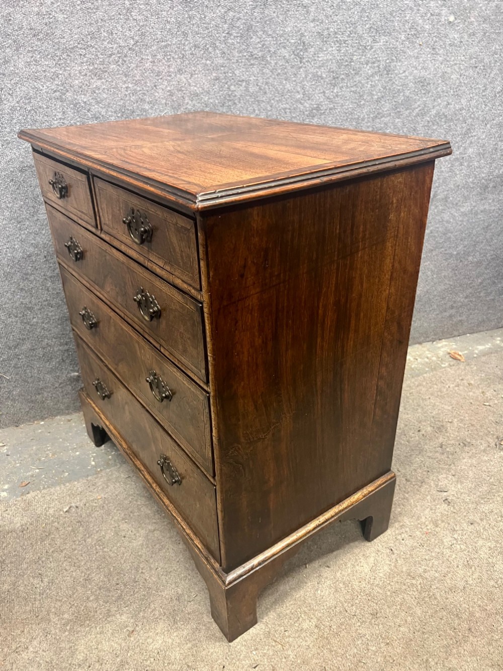 A small 18th-century style walnut chest of drawers featuring figured wood grain, brass drop handles, and bracket feet. View VIII