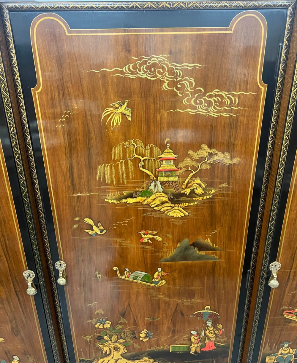 A triple-door Chinoiserie wardrobe featuring intricate gilded Asian landscape scenes, shell-carved crests, and dark polished wood frames. View VI