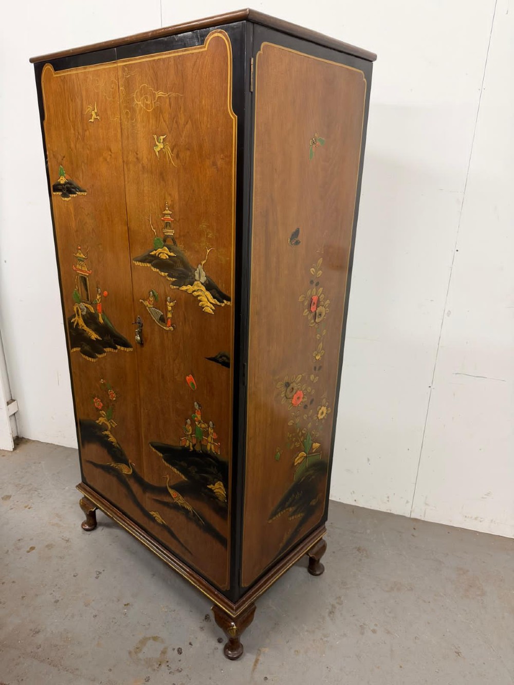 A two-door wooden compactum wardrobe decorated with hand-painted Chinoiserie scenes, pagodas, and figures set within dark lacquered borders. View X