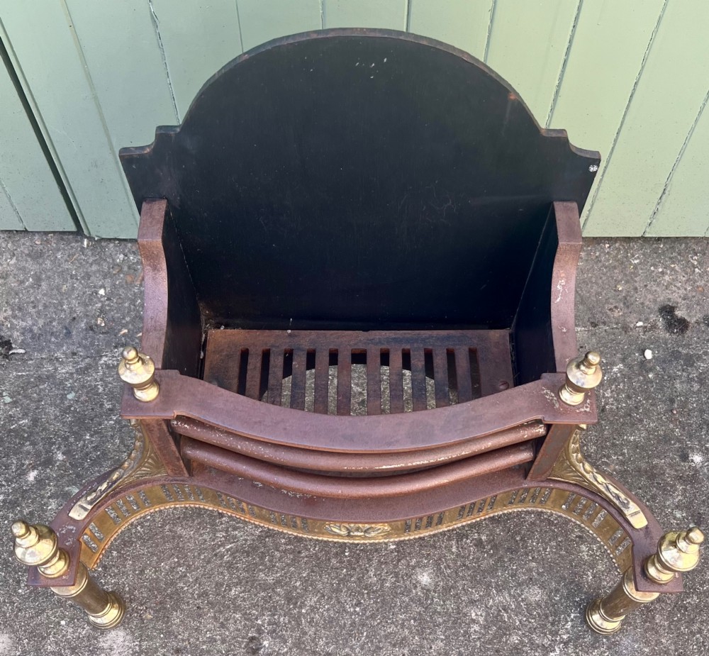 An Adam style brass and cast iron fire grate featuring a serpentine pierced front apron, urn-shaped finials, and a curved black backplate. View II