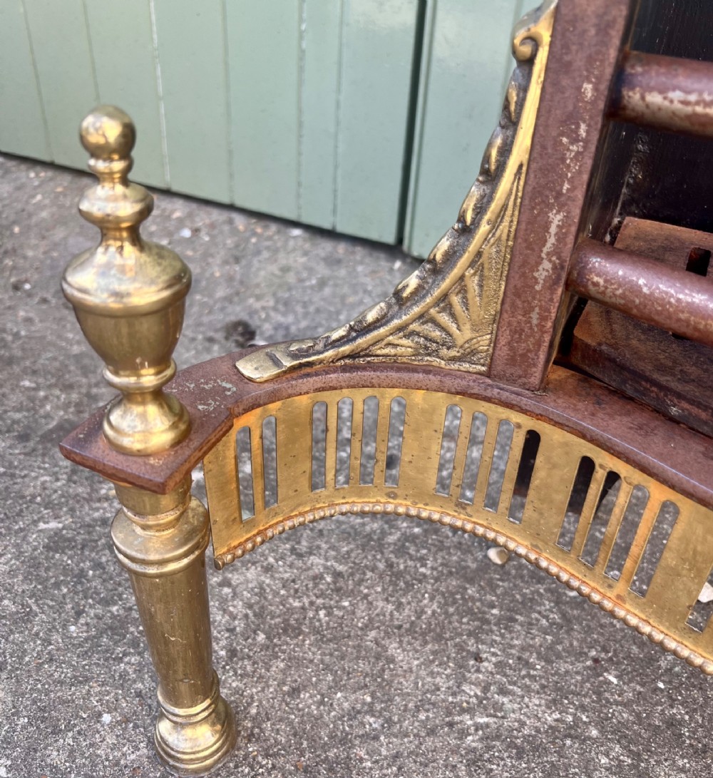 An Adam style brass and cast iron fire grate featuring a serpentine pierced front apron, urn-shaped finials, and a curved black backplate. View IV