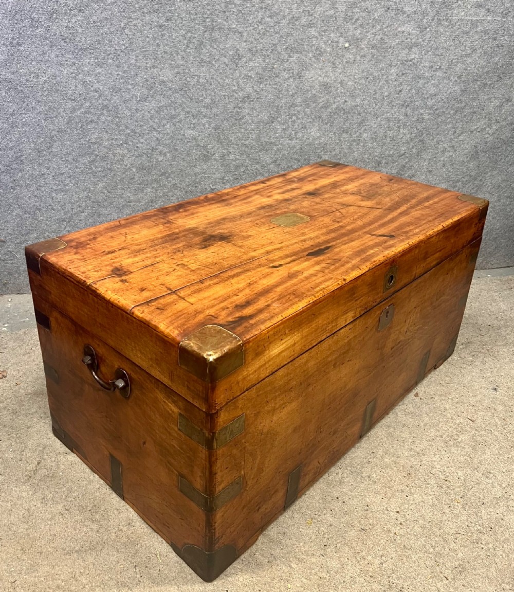 A rectangular Anglo-Indian campaign trunk crafted from warm brown wood with protective brass corner straps and metal carrying handles.