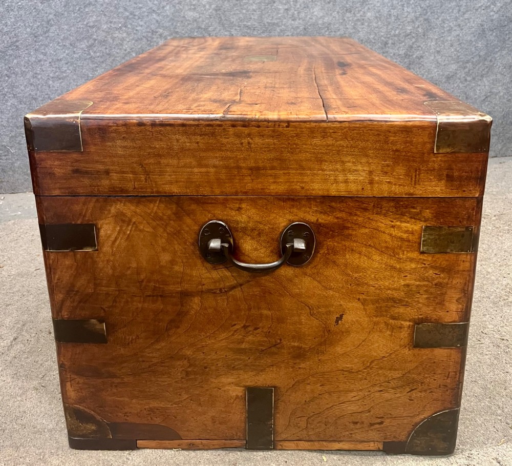 A rectangular Anglo-Indian campaign trunk crafted from warm brown wood with protective brass corner straps and metal carrying handles. View II