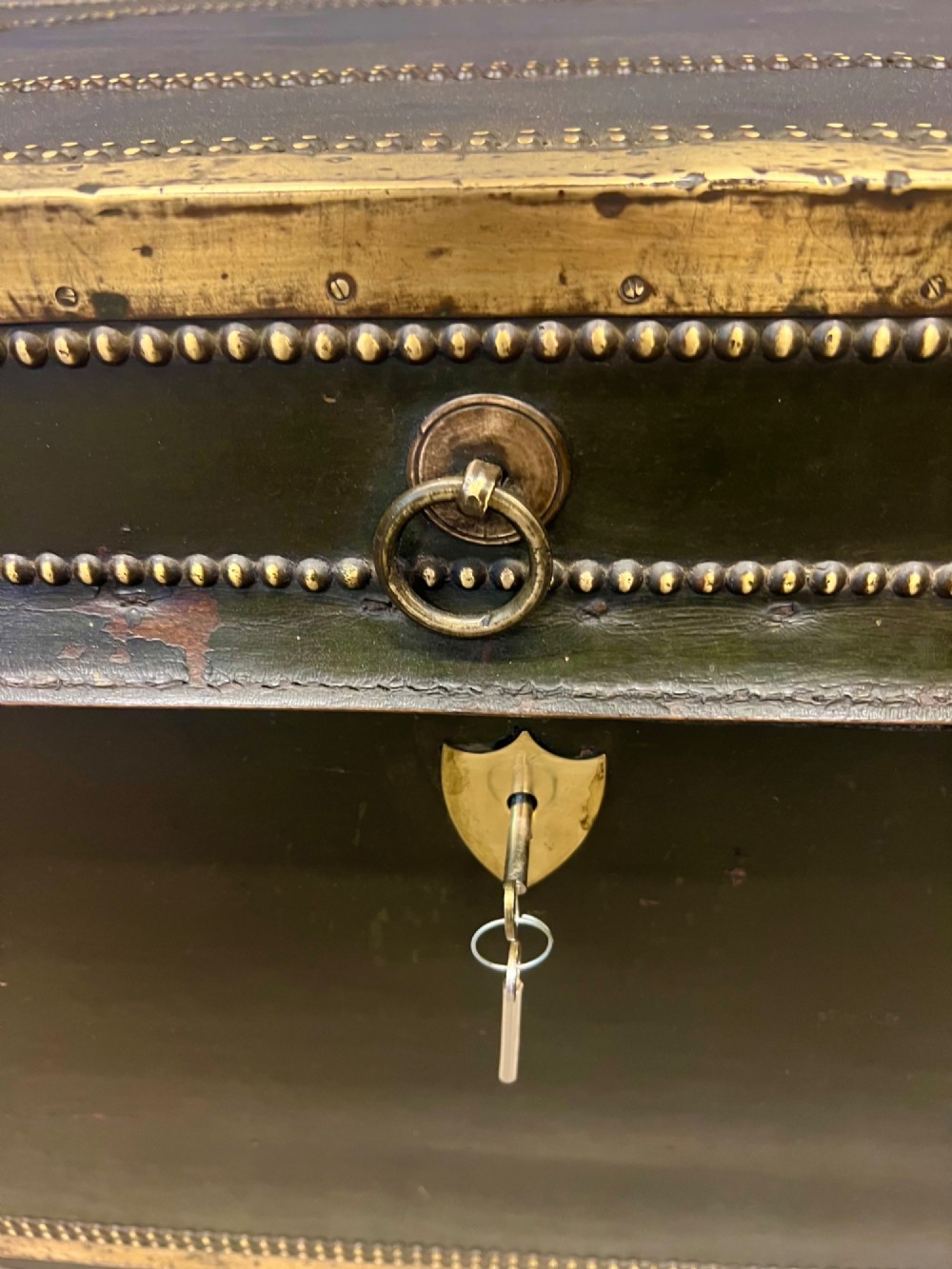 An early nineteenth-century camphor wood campaign trunk wrapped in dark olive green leather with brass stud borders, brass corner plates, side handles, and a key lock. View X