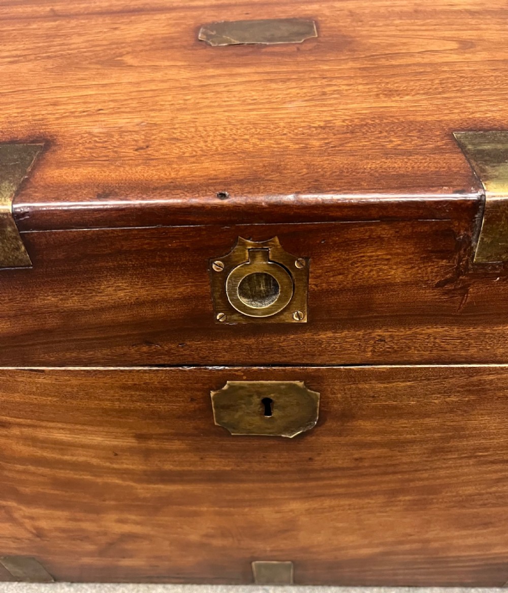 A rectangular warm brown wooden campaign trunk featuring flush brass corner brackets, metal straps, and a central brass lid plaque. View VI