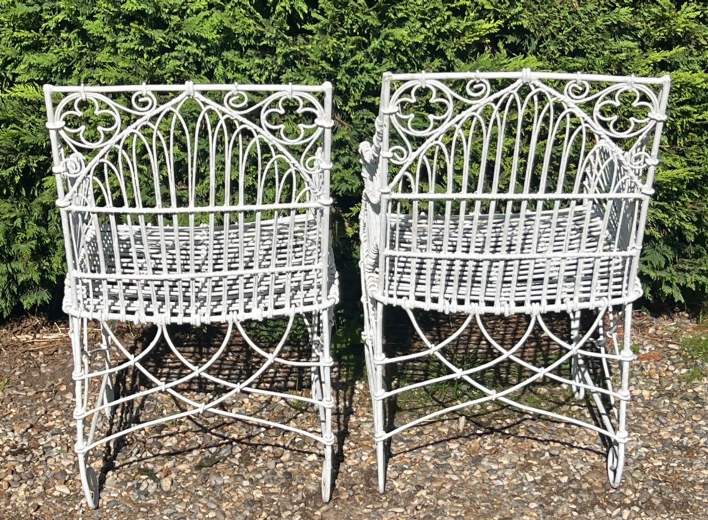 A pair of white painted iron garden chairs featuring Gothic arched backs, slatted wire seats, and scrolled feet. View V