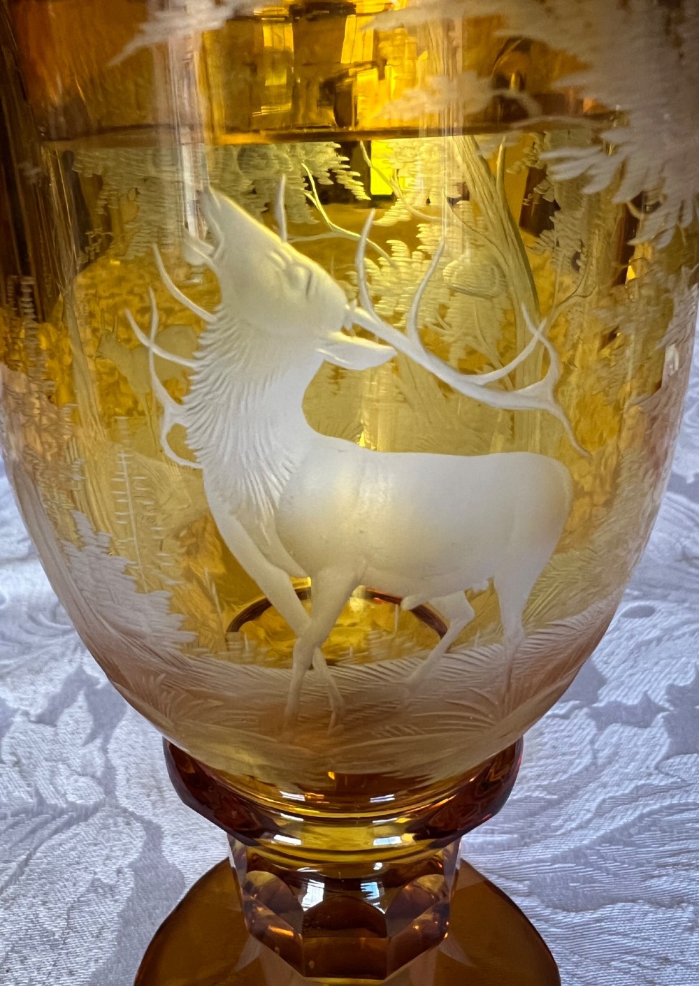 An amber glass lidded pokal vase featuring wheel-engraved woodland imagery with a stag, a faceted stem, and a stepped lid. View II