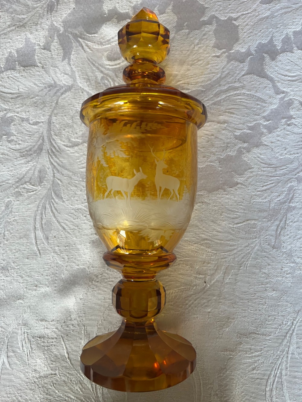 An amber glass lidded pokal vase featuring wheel-engraved woodland imagery with a stag, a faceted stem, and a stepped lid. View III
