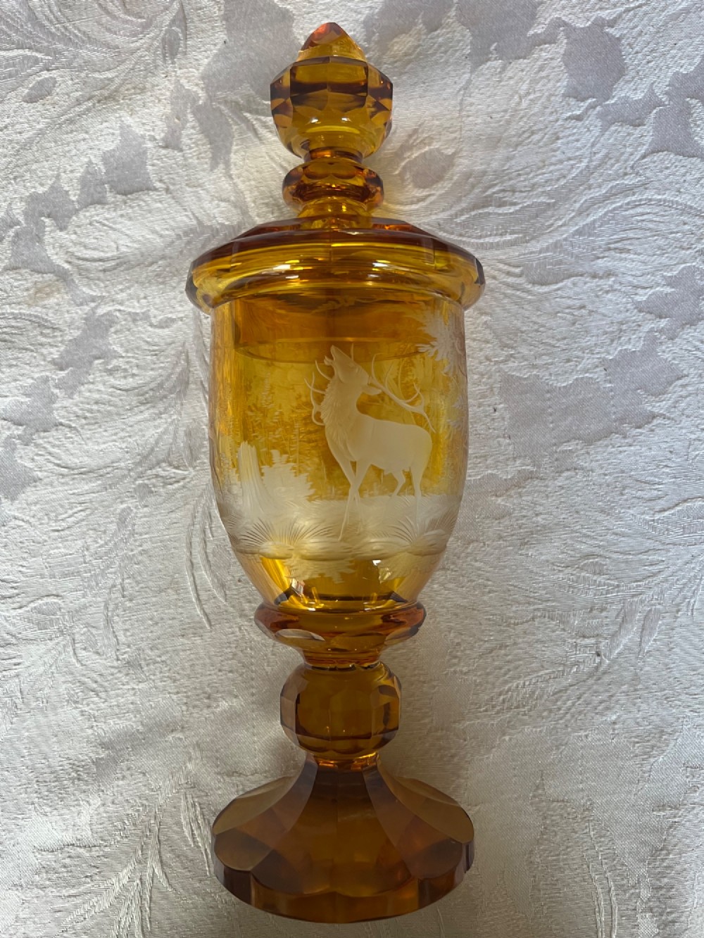 An amber glass lidded pokal vase featuring wheel-engraved woodland imagery with a stag, a faceted stem, and a stepped lid. View IV