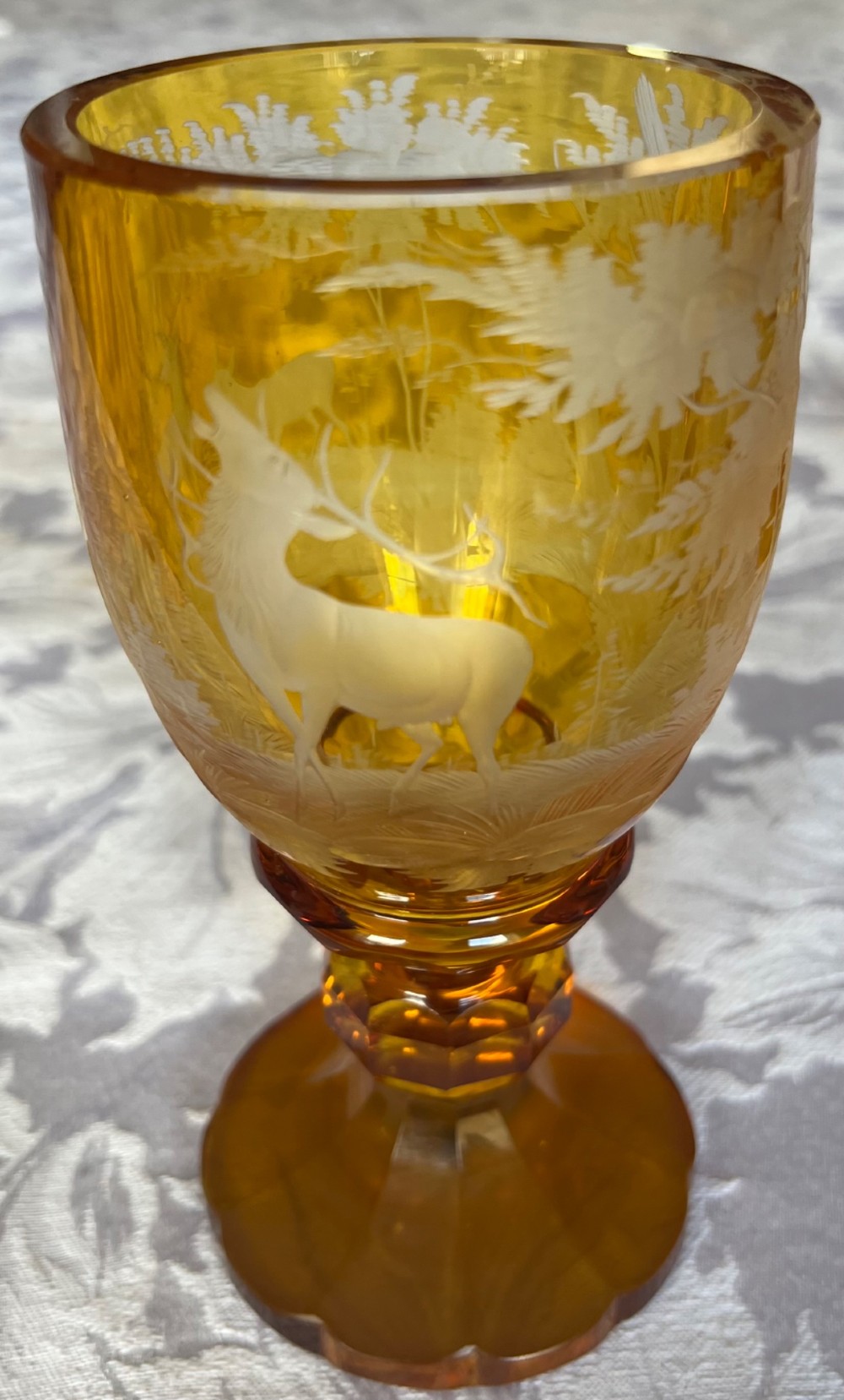 An amber glass lidded pokal vase featuring wheel-engraved woodland imagery with a stag, a faceted stem, and a stepped lid. View V