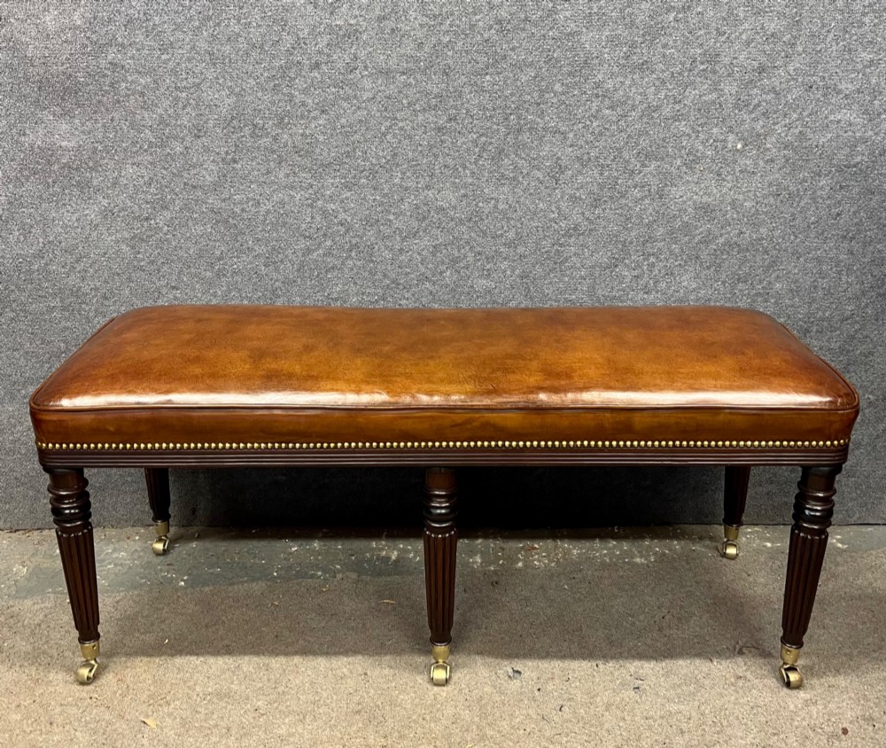 An early nineteenth-century upholstered brown leather bench featuring brass studded trim and six dark wood fluted turned legs on brass castors. View III