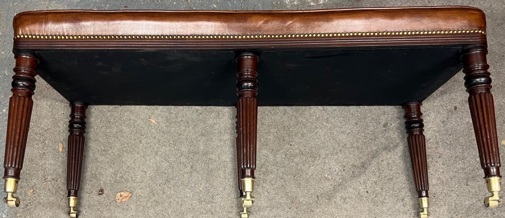 An early nineteenth-century upholstered brown leather bench featuring brass studded trim and six dark wood fluted turned legs on brass castors. View VIII