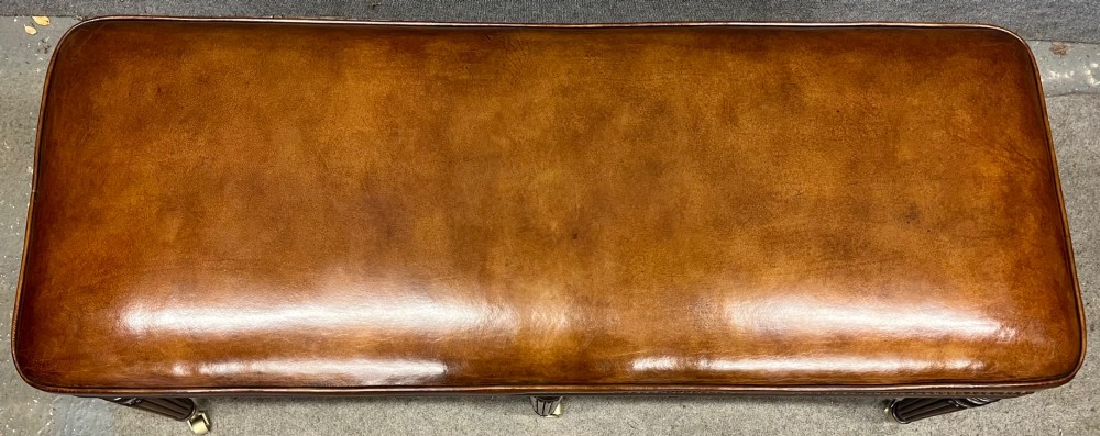An early nineteenth-century upholstered brown leather bench featuring brass studded trim and six dark wood fluted turned legs on brass castors. View IX